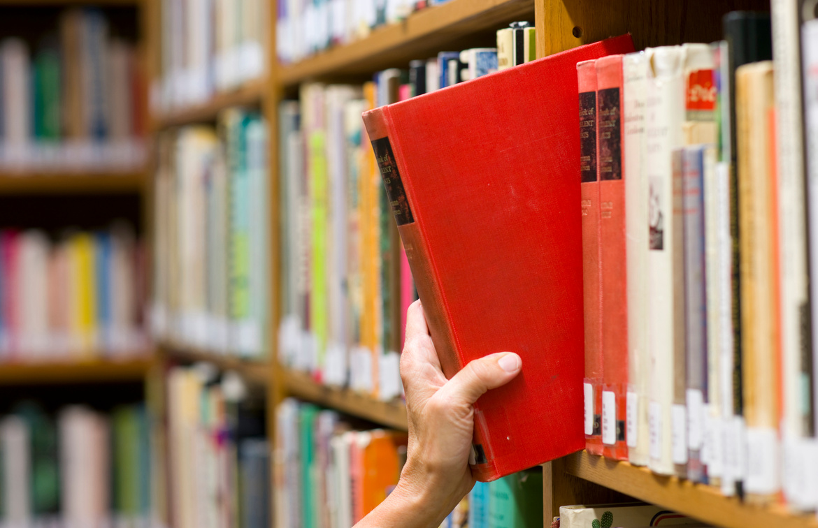 Hand Taking a Book from the Library Shelf